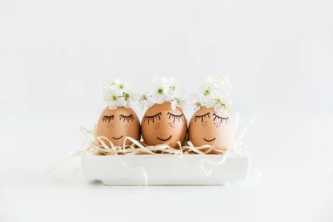 Brown hand drawn eggs with faces in the nest, with blooming flowers. Easter.. Stock Photos