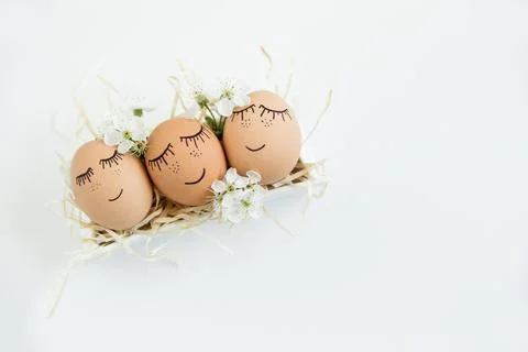Brown hand drawn eggs with faces in the nest, with blooming flowers. Easter.. Stock Photos