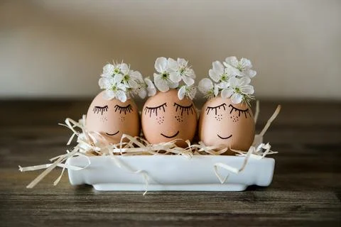 Brown hand drawn eggs with faces in the nest, with blooming flowers. Easter.. Stock Photos