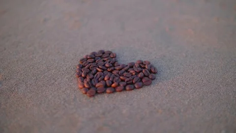 Brown heart made from coffee beans scattered on the beach in sunset light Stock Footage 86327699
