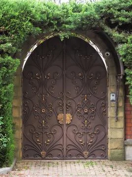 Brown iron gates with a forged pattern of gilded monograms are surrounded by Stock Photos