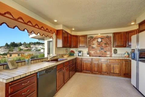 Brown kitchen interior with cabinets, tile counter tops, brick wall, white fr Stock Photos