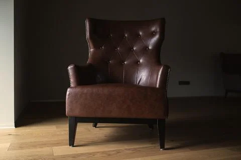 Brown leather armchair in an empty dark room by the window Stock Photos