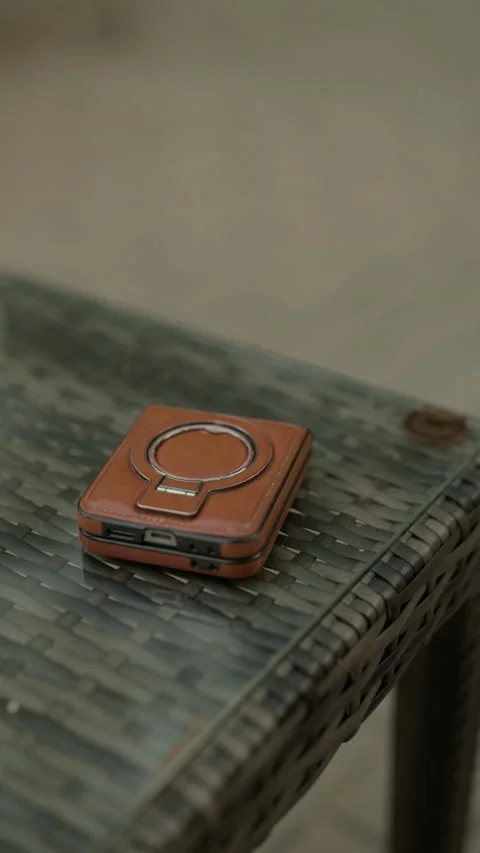 Brown leather compact case with metal ring resting on woven rattan table in soft Stock Footage 345265919
