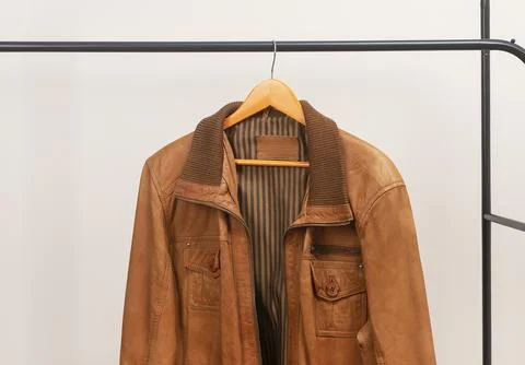 Brown leather jacket hanging on rack with zipper. Outerwear garment placed on Stock Photos
