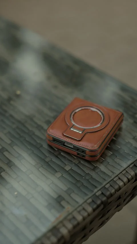 Brown leather phone case with circular magnetic mount resting on woven table Stock Footage 345267588