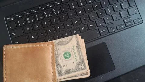 Brown leather wallet with two dollar bills on laptop keyboard Stock Photos