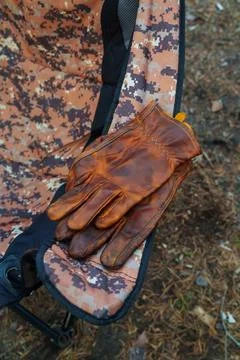 Brown leather work gloves lying on a camouflage camping chair in the forest. Stock Photos