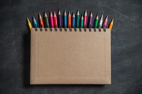 Brown notebook lies on a set of multi-colored pencils on a dark background Stock Photos