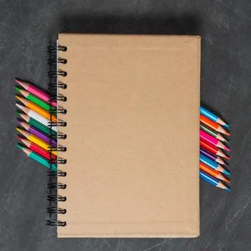 Brown notebook lies on a set of multi-colored pencils on a dark background Stock Photos