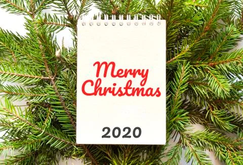Brown notepad lying on branches of a christmas tree with text Merry Christmas Stock Photos