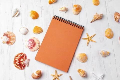 Brown open notepad surrounded by sea shells on white wooden table closeup Stock Photos