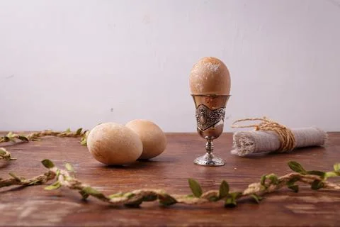 Brown painted Easter egg in silver egg cup on rustic table, white background. Stock Photos