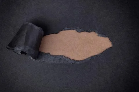 Brown paper background appearing behind torn black paper Stock Photos