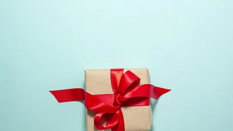 Brown paper gift box with a red ribbon bow fall down on blue background Stock Footage