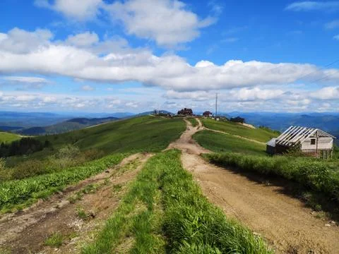 Brown paths along green hills peaks with wooden houses on the top. Stock Photos