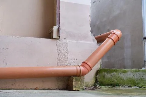 A brown plastic sewer pipe comes around the corner and runs along the wall. Stock Photos