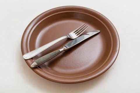 Brown plate with parallel knife, spoon on white Foto stock