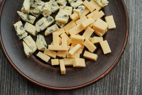 Brown plate on which two types of cheese cut into cubes. one with blue mold the  Stock Photos