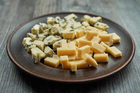 Brown plate on which two types of cheese cut into cubes. one with blue mold the  Stock Photos