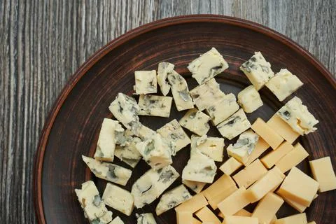 Brown plate on which two types of cheese cut into cubes. one with blue mold  Stock Photos