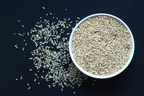 Brown rice grains in a white bowl on a dark background, seen from above Stock Photos