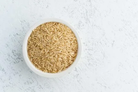 Brown rice in white bowl on white background. Dried cereals in cup, Stock Photos