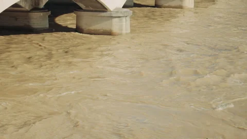 Brown river water flows swiftly under a stone bridge, creating an action 스톡 동영상 313455225