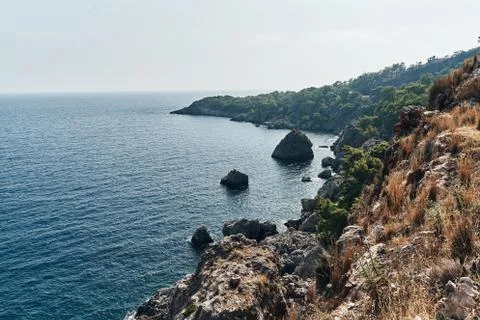Brown rocks and sharp stones in the greenish blue water of Aegean sea near the Stock Photos