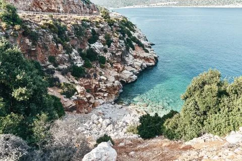 Brown rocks and sharp stones in the greenish blue water of Aegean sea near the Stock Photos