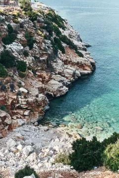 Brown rocks and sharp stones in the greenish blue water of Aegean sea near the Stock Photos