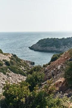 Brown rocks and sharp stones in the greenish blue water of Aegean sea near the Stock Photos