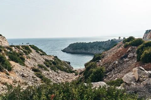 Brown rocks and sharp stones in the greenish blue water of Aegean sea near the Stock Photos