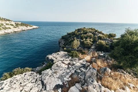 Brown rocks and sharp stones in the greenish blue water of Aegean sea near the Stock Photos