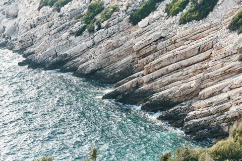 Brown rocks and sharp stones in the greenish blue water of Aegean sea near the Stock Photos