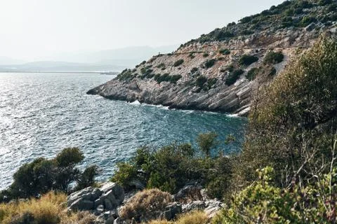 Brown rocks and sharp stones in the greenish blue water of Aegean sea near the Stock Photos