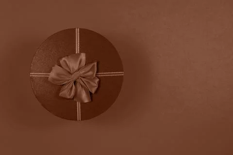 Brown round gift box with a bow on a mocha mousse color background. Stock Photos