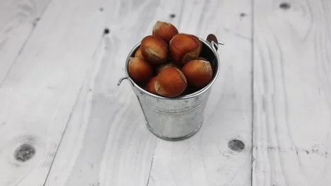 Brown-shelled hazelnuts lying in a small bucket rotate on a wooden table. FullHD Vídeo Stock 147087549