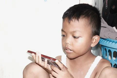 A brown-skinned boy in a singlet is playing with his cell phone Foto stock