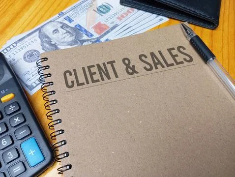 Brown spiral notebook with Client &amp; Sales text on a wooden desk with a calc.. Stock Photos