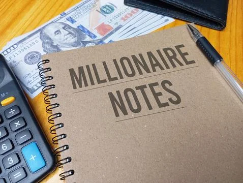 Brown spiral notebook with Millionaire Notes text on a wooden desk with a c.. Stock Photos
