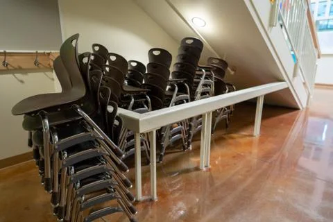 Brown stacking chairs at a school setting piled under stairs Stock Photos