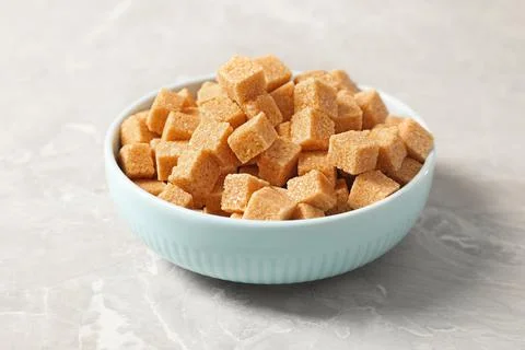 Brown sugar cubes in bowl on light grey marble table Stock Photos