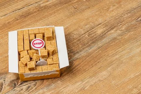 Brown sugar cubes in a box with a stop sign on a wooden surface Stock Photos