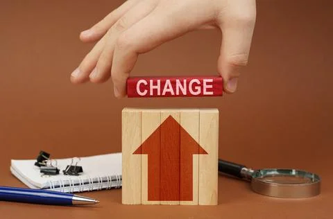 On a brown surface are office items, wooden blocks, in the hand is a red bloc Stock Photos