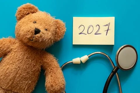 Brown teddy bear lying on blue background next to stethoscope and paper with Foto stock