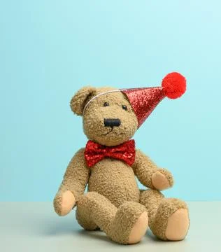 Brown teddy bear in a red cap sits on a blue background, Stock Photos