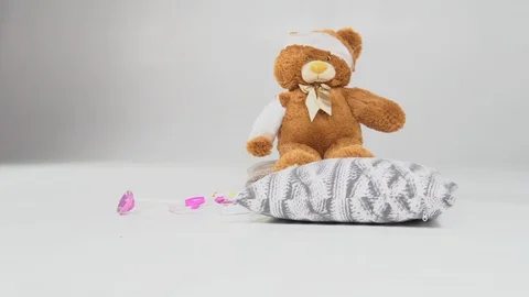 Brown teddy bear with rewound white bandage paw on a white wooden background Stock Footage 127639769