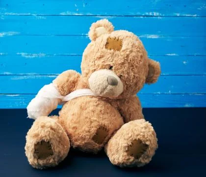 Brown teddy bear with rewound white bandage paw on a blue wooden background Stock Photos