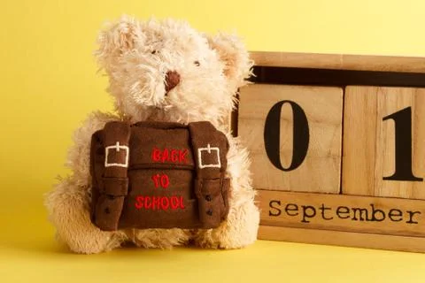 Brown teddy bear with school backpack and decoratibe wooden calendar, yellow  Stock-Fotos